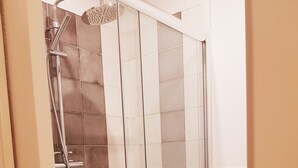 A glass-enclosed shower stall with a tiled wall and a white toilet visible to the right. - Cairoli Rooms (Rome)