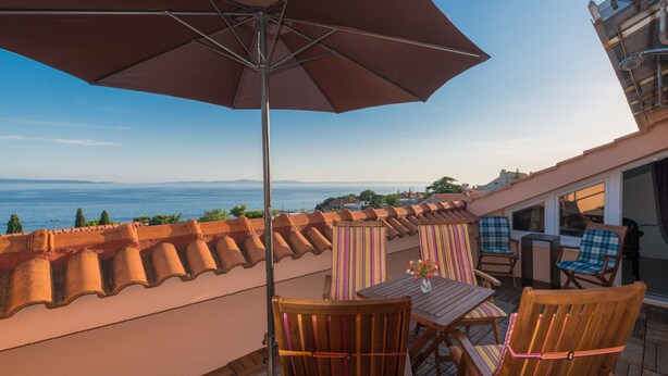 Une terrasse avec des meubles en bois, une table ornée d’un vase et un grand parasol.
