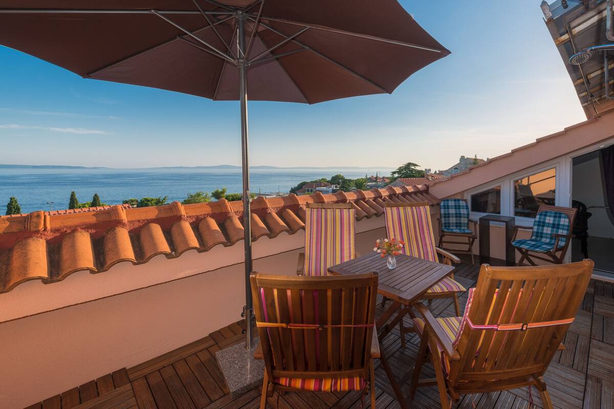 Eine Terrasse mit Holzmöbeln, einem Tisch mit einer Vase und einem großen Sonnenschirm.