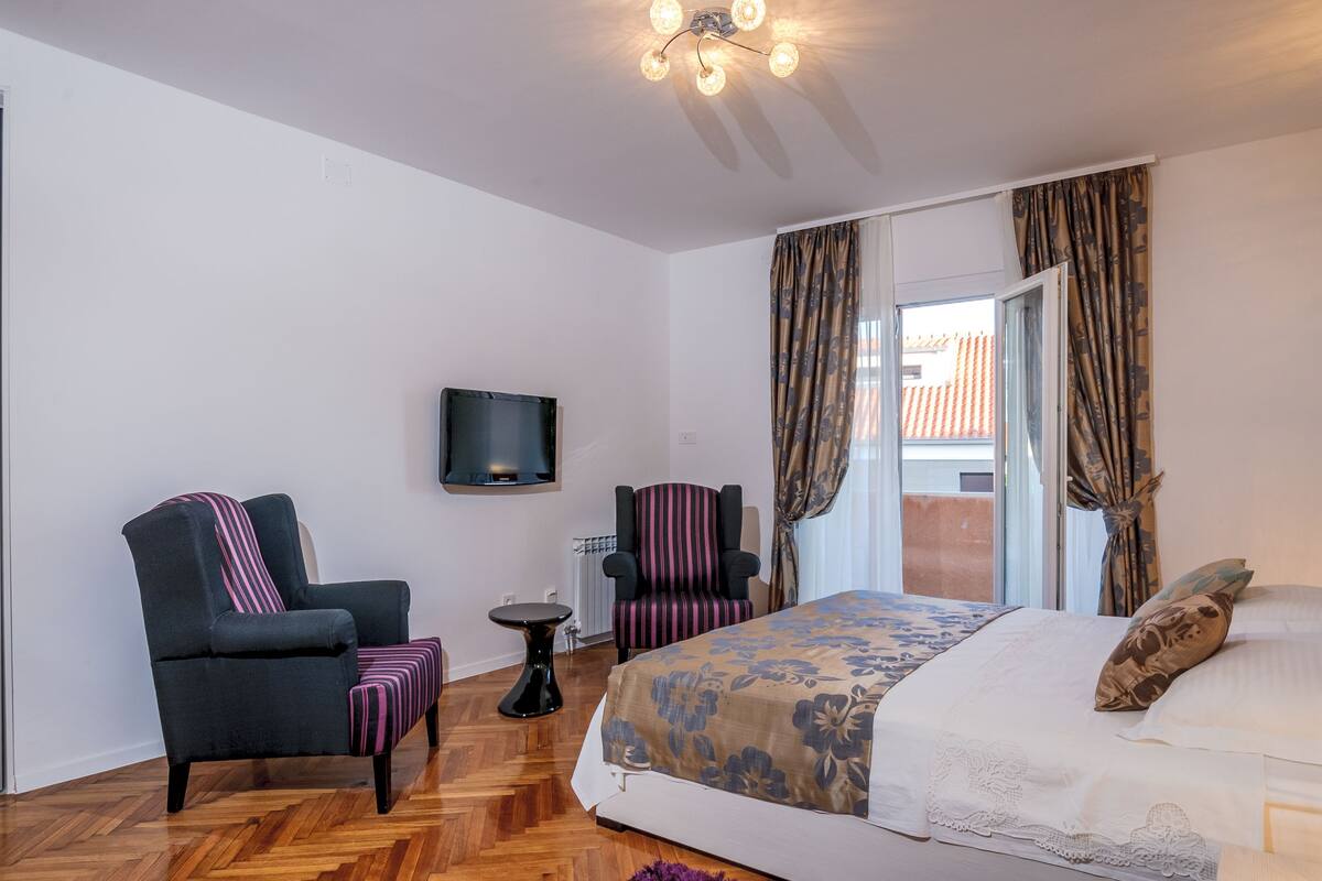 Ein Hotelzimmer mit einem Bett, zwei Sesseln, einem kleinen Tisch, einem Fernseher und einem Fenster mit Vorhängen.