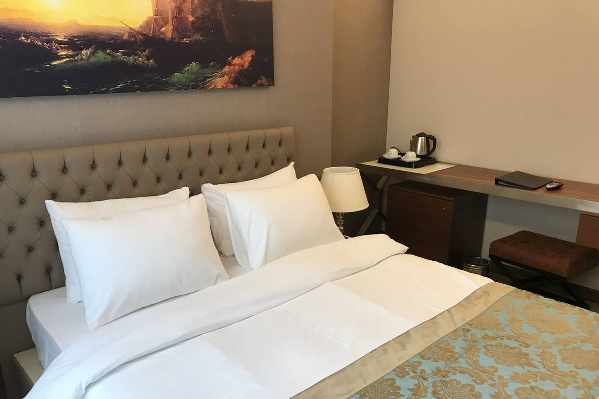 A neatly made bed with white linens, a tufted headboard, and a patterned bedspread.