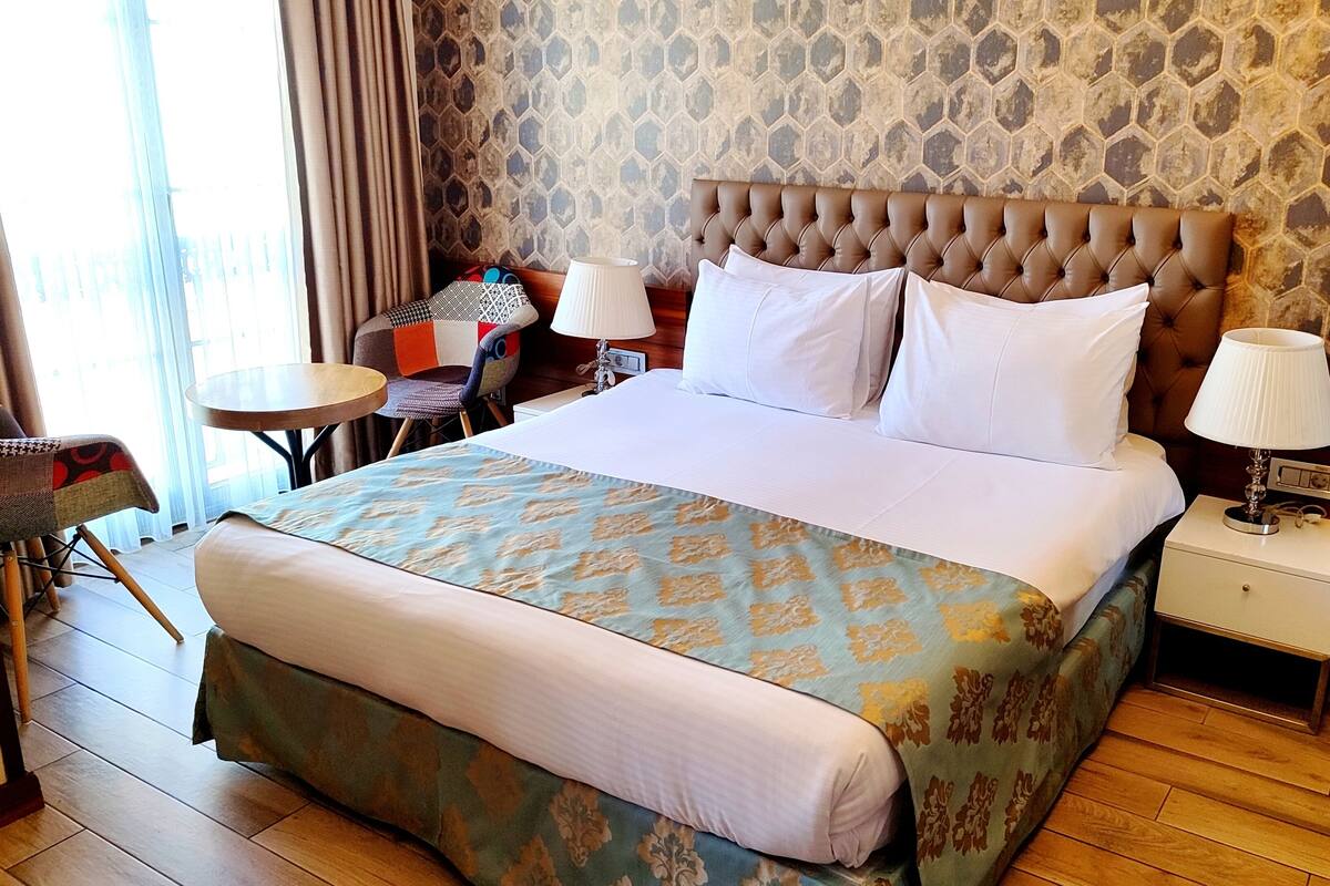 A hotel room with a large bed, a bedside table with a lamp, a chair, and a small table.