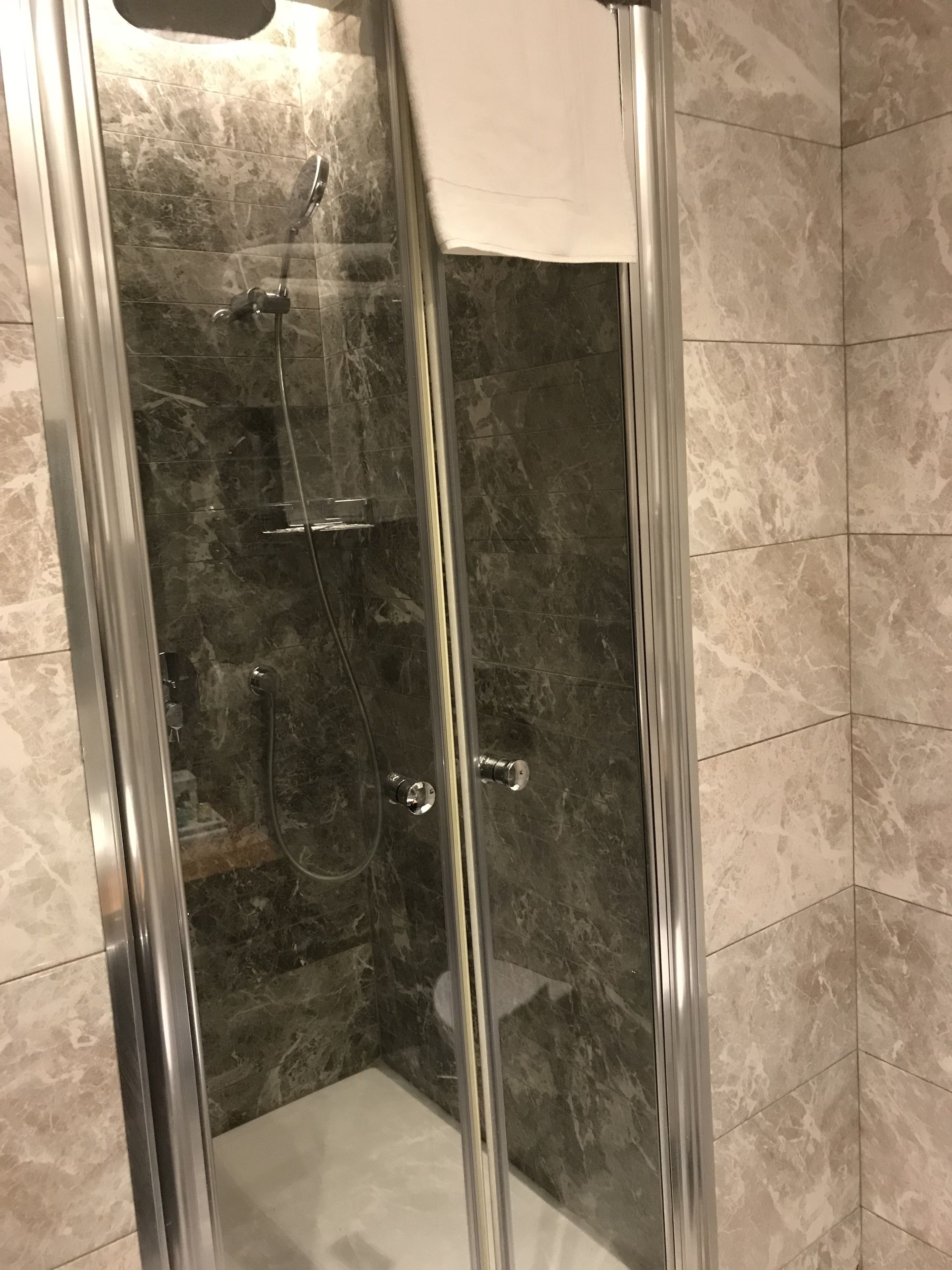 A glass-enclosed shower stall with a handheld showerhead and a wall-mounted faucet.
