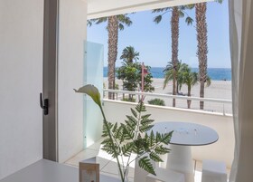 Un balcón con vista a la playa, palmeras y un cielo despejado.