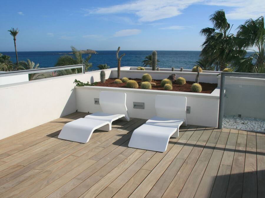 A wooden deck with white lounge chairs and a planter with cacti and succulents.
