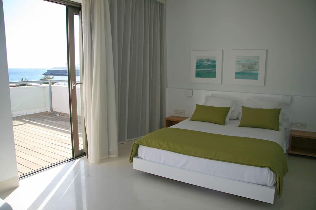 A bedroom with a bed, a nightstand, a window with curtains, and two framed pictures on the wall.