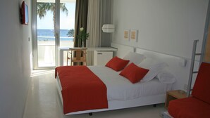 Habitación de hotel con cama, escritorio, silla, una mesita y vista al océano.