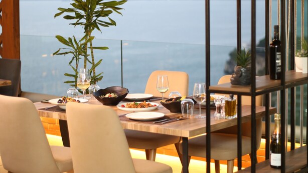 Un comedor con una mesa lista para dos personas, una planta en maceta y vistas al mar.