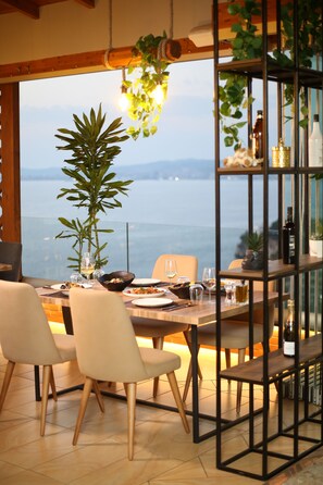 Un comedor con una mesa lista para dos personas, una planta en maceta y vistas al mar.