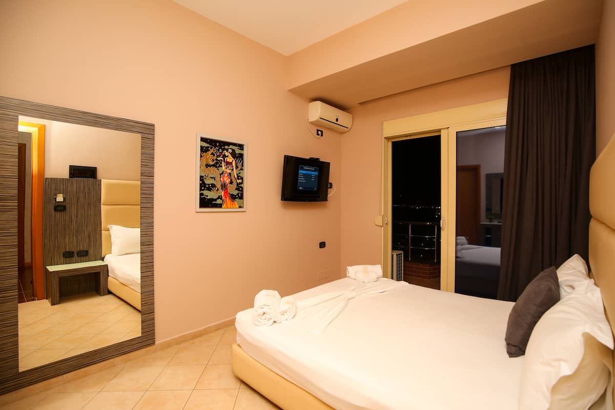 A hotel room with a large bed, a television, a mirror, and a door leading to a balcony.