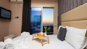 Habitación de hotel con cama, mesita de noche con bandeja de desayuno, televisor y vista al atardecer por la ventana.