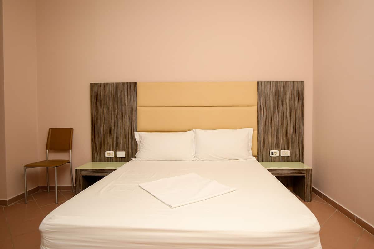 A hotel room with a large bed, two nightstands, a chair, and a headboard with vertical lines.