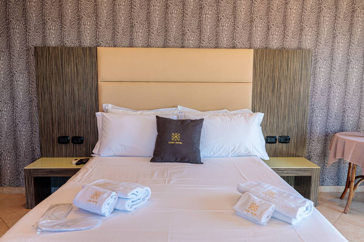 A hotel room with a large bed, a headboard, two bedside tables, and a small table with a chair.