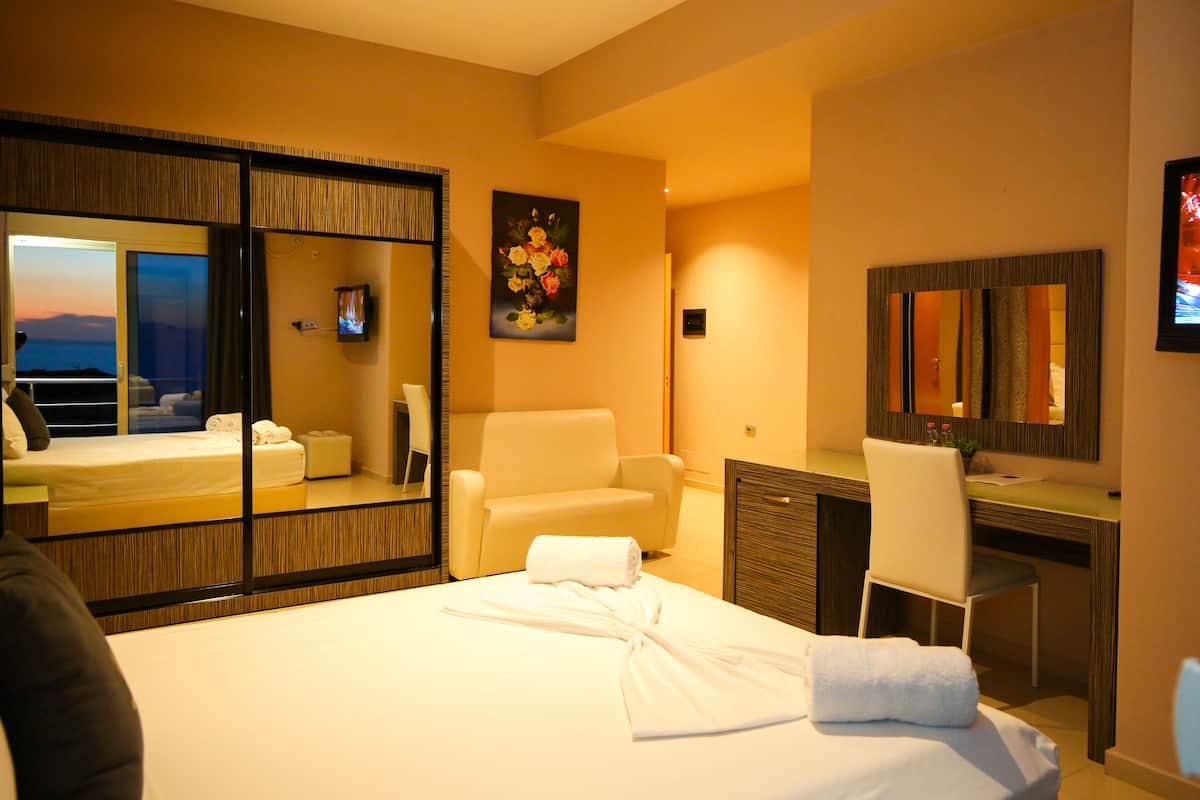 A hotel room with a bed, a desk, a chair, a large mirror, and a painting on the wall.