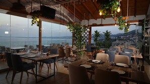 Un restaurante con vistas al mar, amplios ventanales y plantas colgantes.
