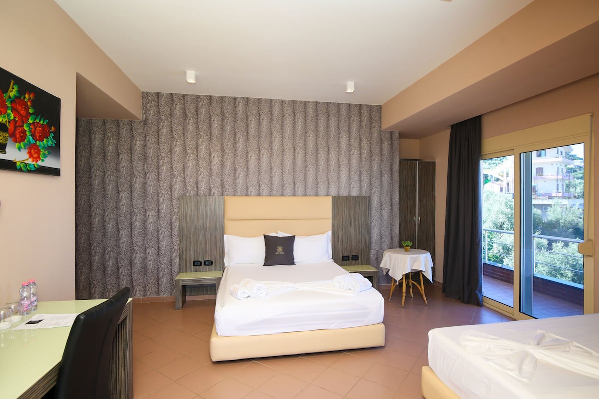 A hotel room with a large bed, a small table, a chair, and a balcony with a view.