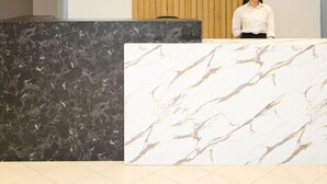 Un mostrador de recepción con encimera de mármol, pared revestida de madera y una lámpara de techo moderna.