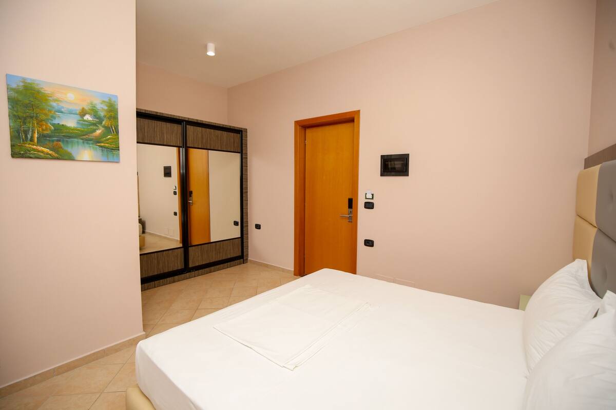 A bedroom with a bed, a wardrobe, a door, and a painting on the wall.