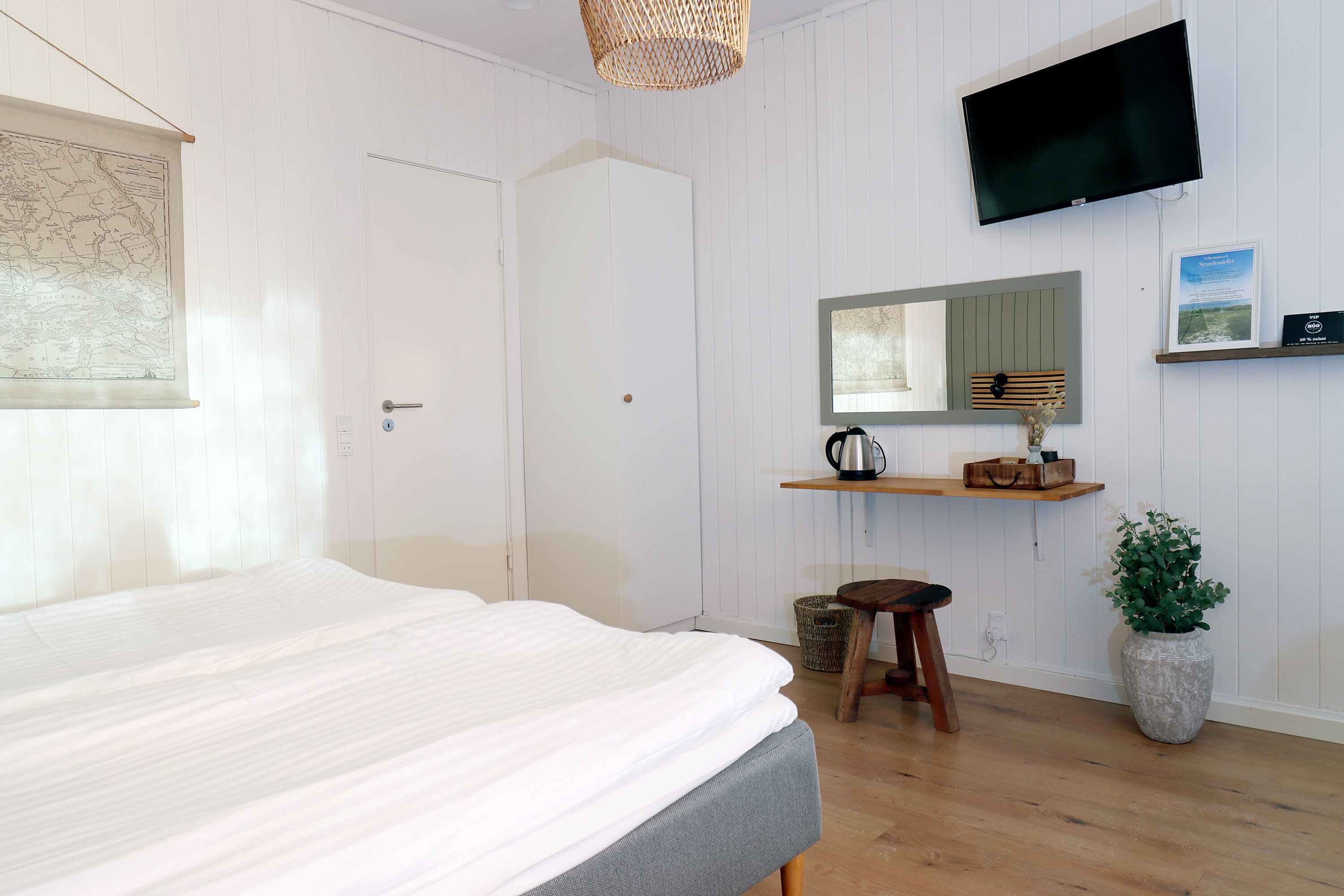 Een slaapkamer met een bed, een televisie, een bureau met spiegel en een potplant.