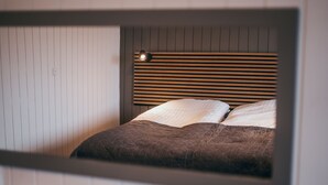 Un dormitorio con una cama, cabecera de listones horizontales y una lámpara fijada a la pared.