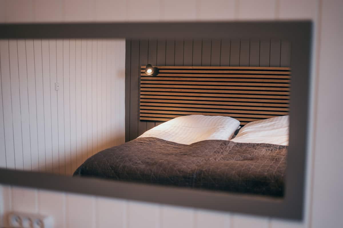 A bedroom with a bed, a headboard with horizontal slats, and a wall-mounted light fixture.