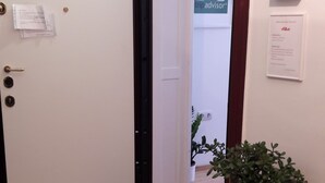 Entrada de hotel con puerta cerrada, felpudo y planta en maceta, indicando que el hotel está abierto.