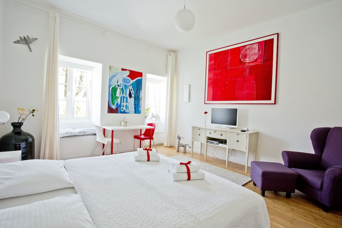 Ein Hotelzimmer mit einem großen Bett, einem Schreibtisch mit Computer, einem Fernseher und einem violetten Sessel.