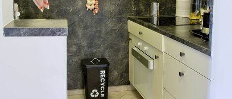 Una cocina con armarios blancos, salpicadero de mármol y un contenedor negro para reciclaje.