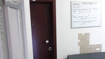 A room with a wooden door, a reception sign, a welcome mat, a bench, and a wall-mounted sign with text.