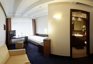 A hotel room with a bed, a desk with a computer, a chair, a small table, and a bathroom with a sink and mirror. - Hotel Silicium (Hoehr-Grenzhausen)