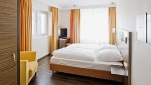 A hotel room with a wooden ceiling, a bed, a TV, and a yellow armchair.