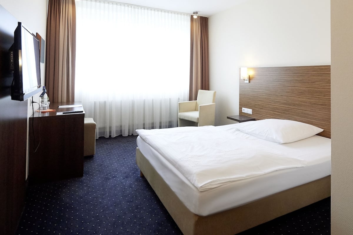 Una habitación de hotel con una cama, un escritorio con silla, un televisor y una ventana con cortinas.