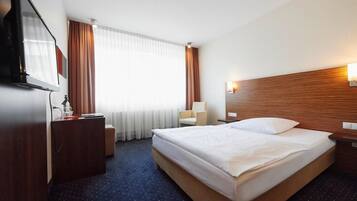 Ein Hotelzimmer mit einem großen Bett, einem Schreibtisch mit Stuhl, einem Fernseher und einem Fenster mit Vorhängen.
