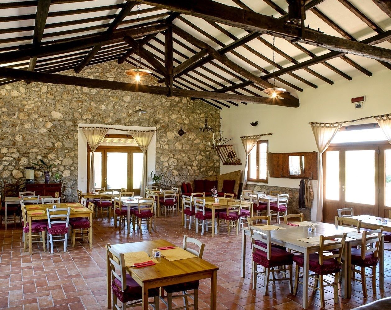 A rustic dining area with stone walls, wooden beams, and multiple tables and chairs.