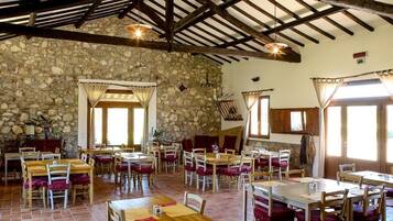 A rustic dining area with stone walls, wooden beams, and multiple tables and chairs.