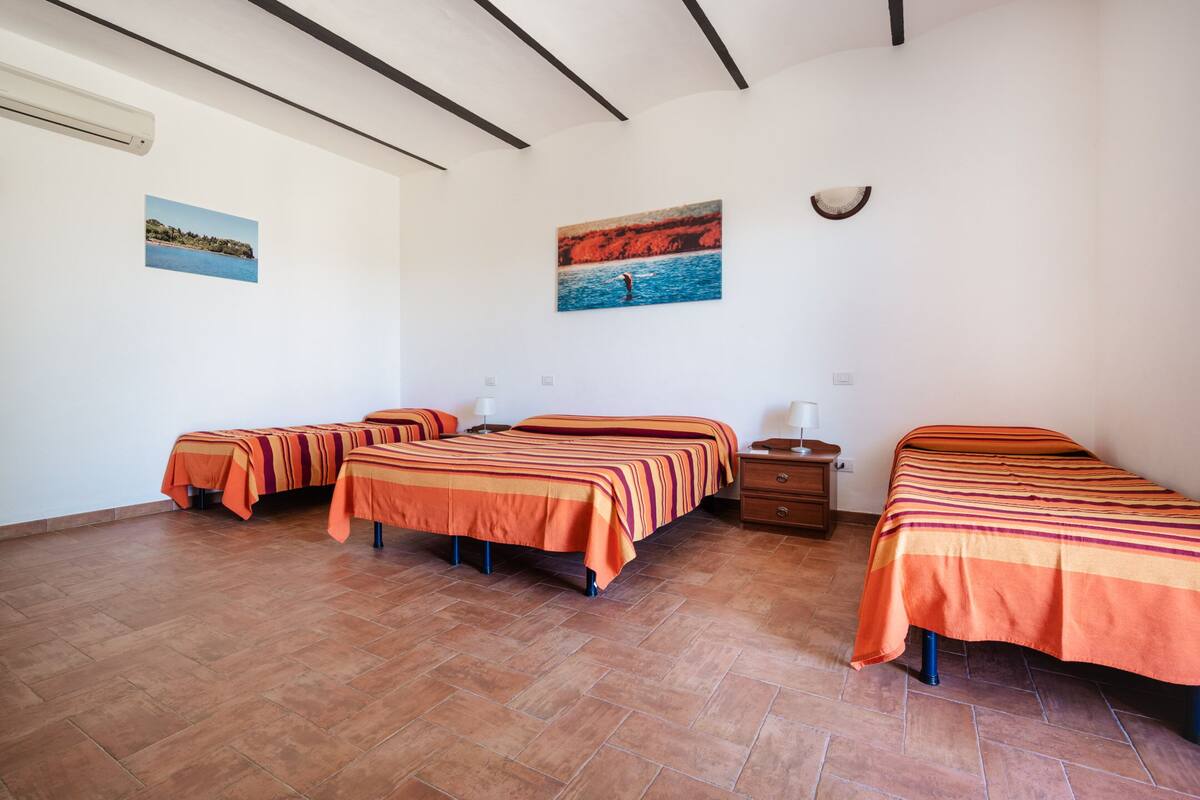 A hotel room with three beds, a tiled floor, and two paintings on the walls.