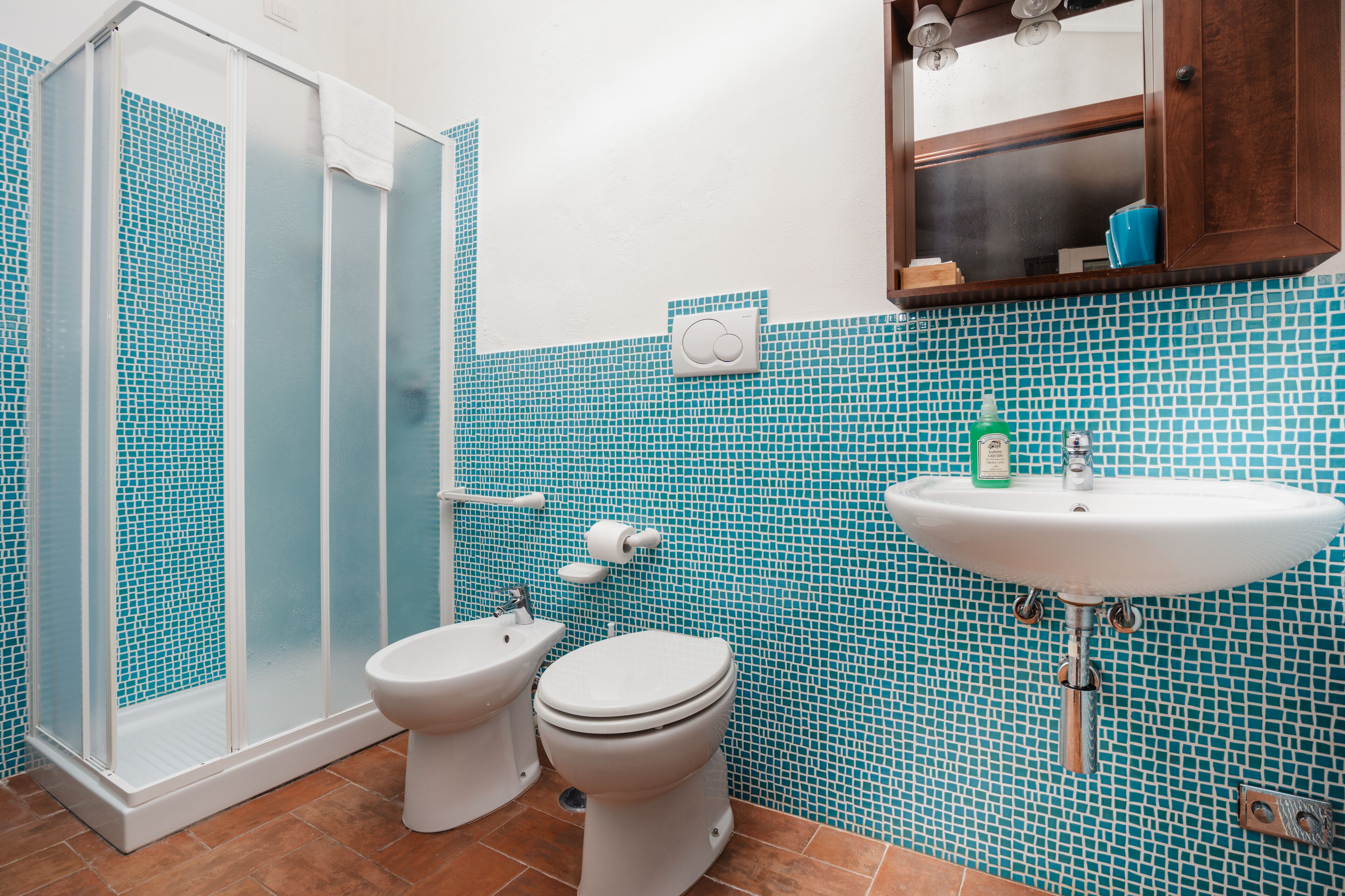 A bathroom with a shower, toilet, sink, and blue mosaic tiles.