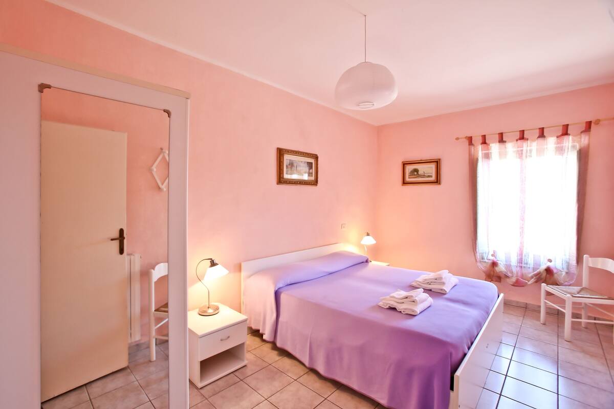 A bedroom with a bed, bedside lamps, a chair, and a window with curtains.