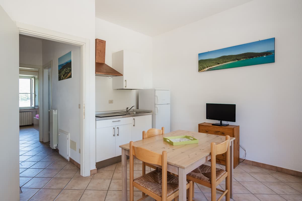 A compact kitchen with white cabinets, a wooden table, and a TV on a small stand.