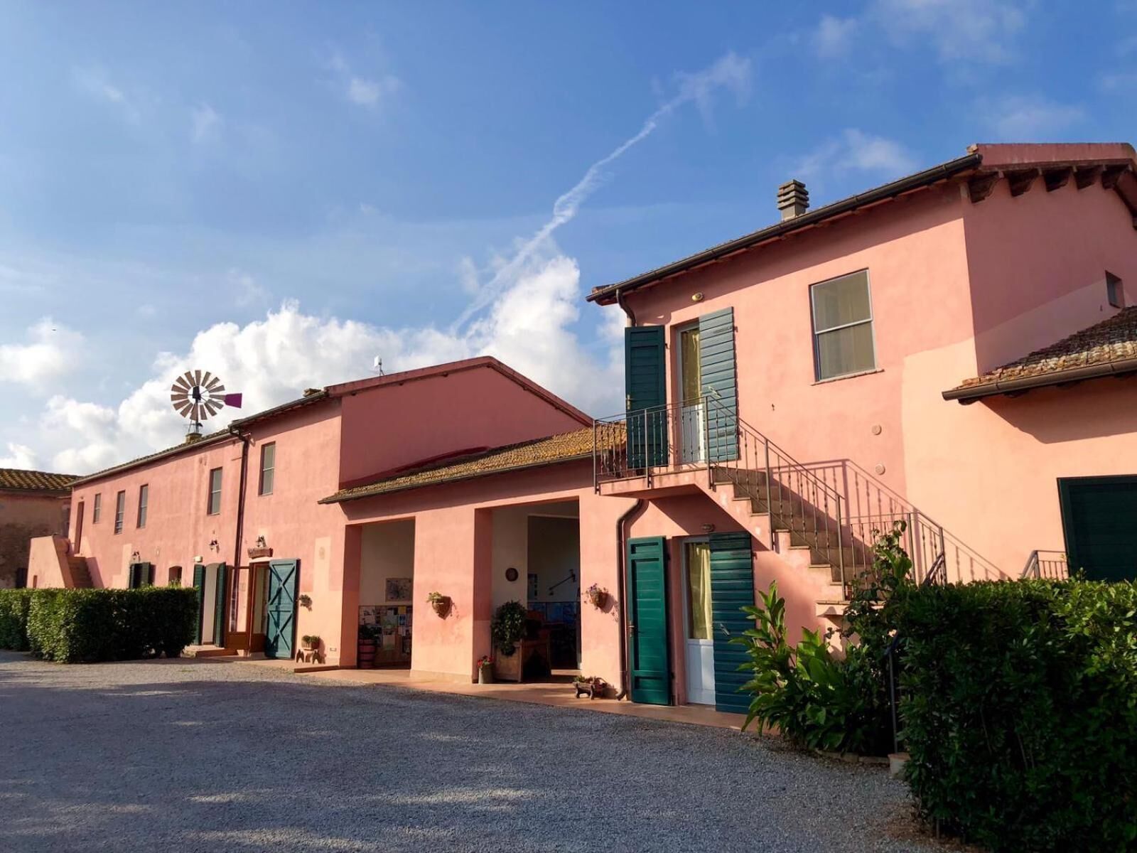 A pink building with a windmill, a staircase, and a gravel driveway.
