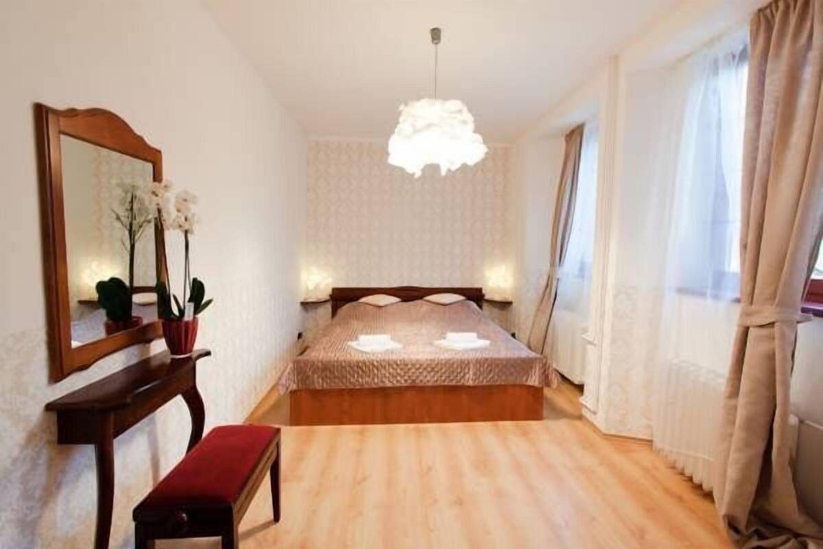 Ein Schlafzimmer mit einem hölzernen Bett, einem Nachttisch, einem Spiegel, einer Pendelleuchte und einem Fenster mit Vorhängen.