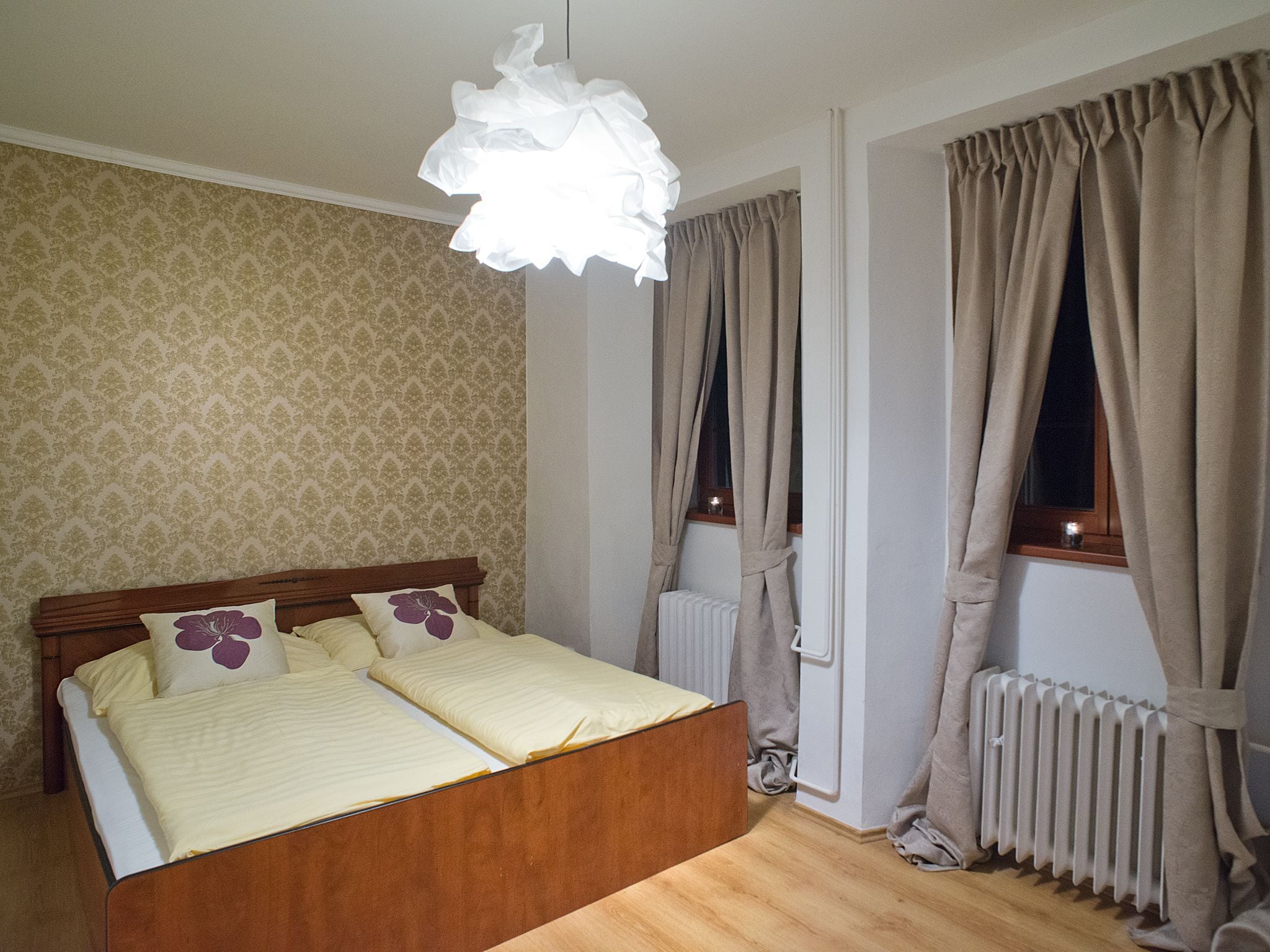 A bedroom with a wooden bed, patterned wallpaper, a radiator, and curtains.