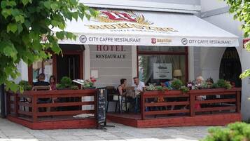 Ein Stadtcafé-Restaurant mit Außenbereich, einem Schild, das es als Hotelrestaurant kennzeichnet, und einer sichtbaren Speisekarte.