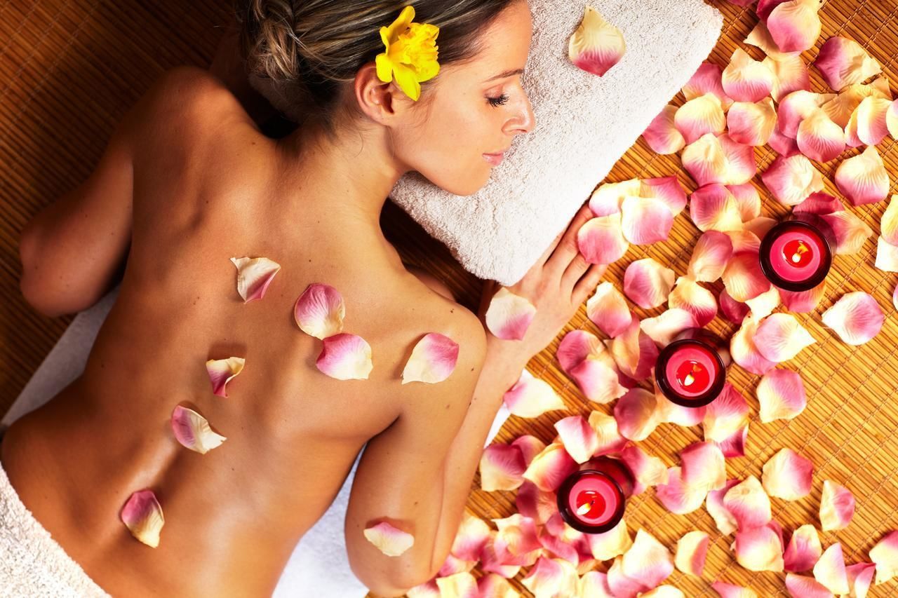 A person lying on a bed with rose petals and candles, suggesting a spa setting.
