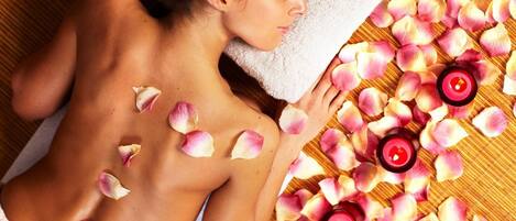 A person lying on a bed with rose petals and candles, suggesting a spa setting.