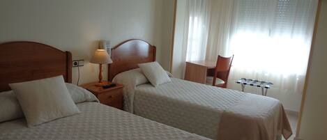 A hotel room with two beds, a desk, a chair, a lamp, and a telephone.