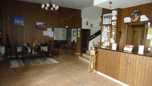 A reception area with a wooden reception desk, a staircase, and a living room with a sofa and a coffee table. - As Maceiras (Puebla de Trives)