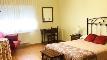 A bedroom with a bed, a desk, a chair, a nightstand, a lamp, a mirror, and a window with curtains.