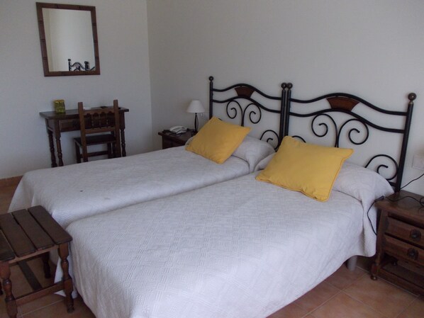 A double bed with two pillows, a nightstand, a bedside table, a mirror, and a small wooden table with a lamp. - As Maceiras (Puebla de Trives)