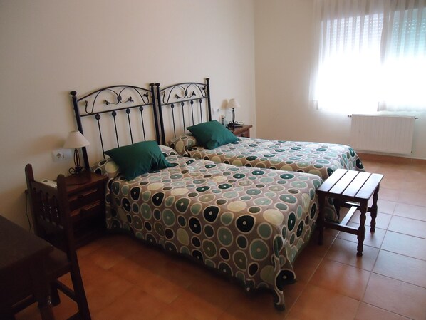 A bedroom with two beds, a wooden table, and a chair. - As Maceiras (Puebla de Trives)